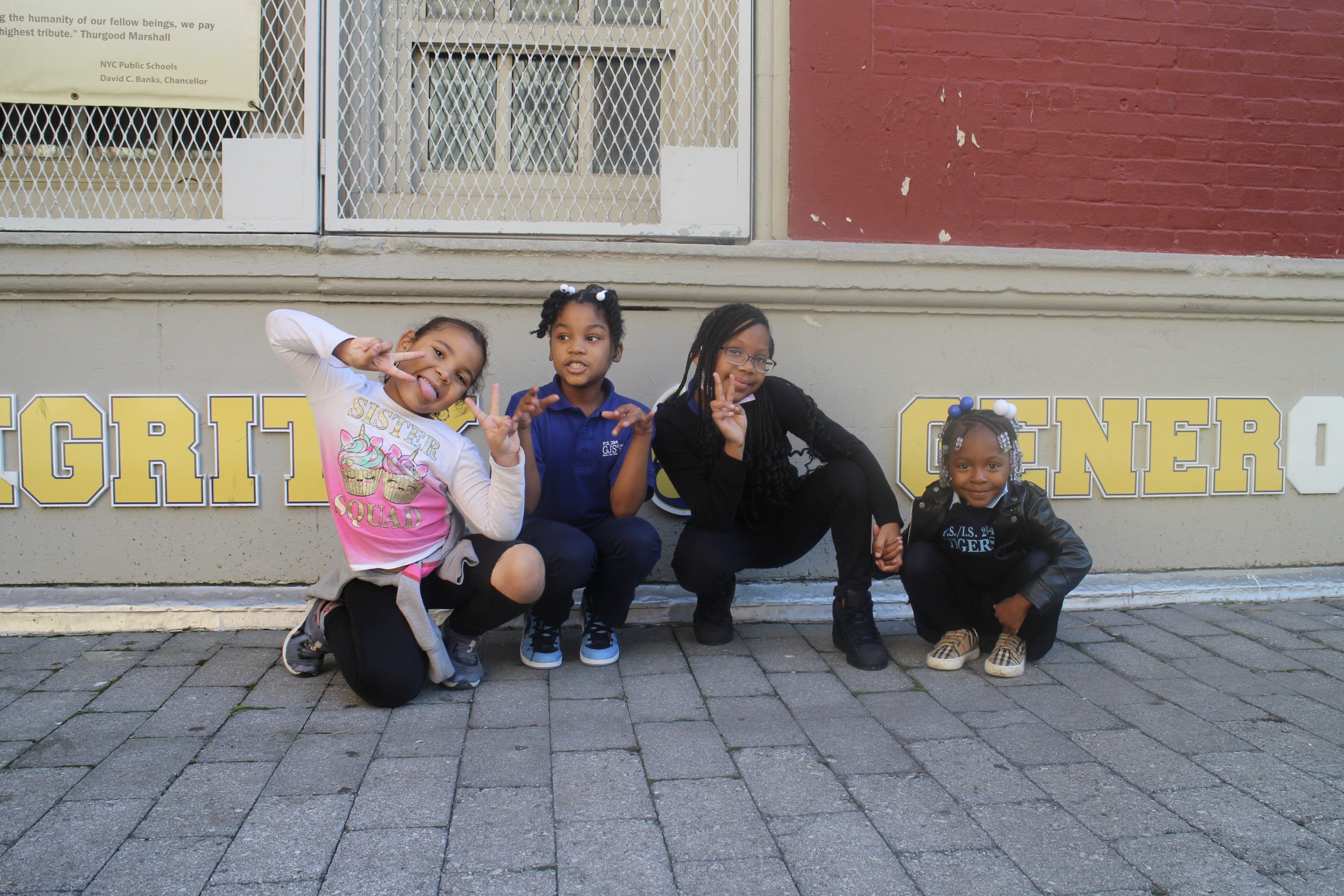 Four young girls crouched down in front of their school making 